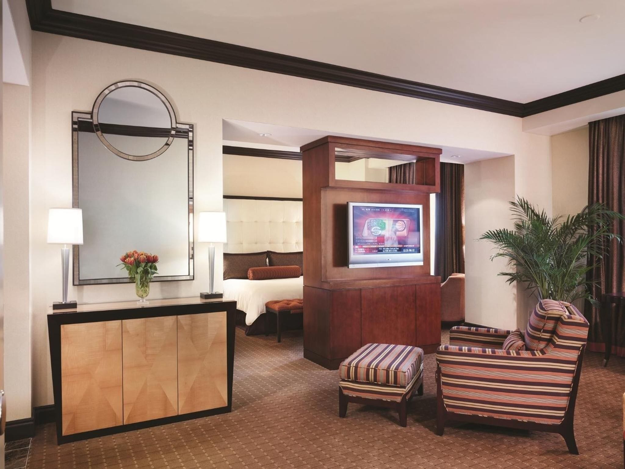A hotel room with a wooden desk, a television, a sofa, and a potted plant.