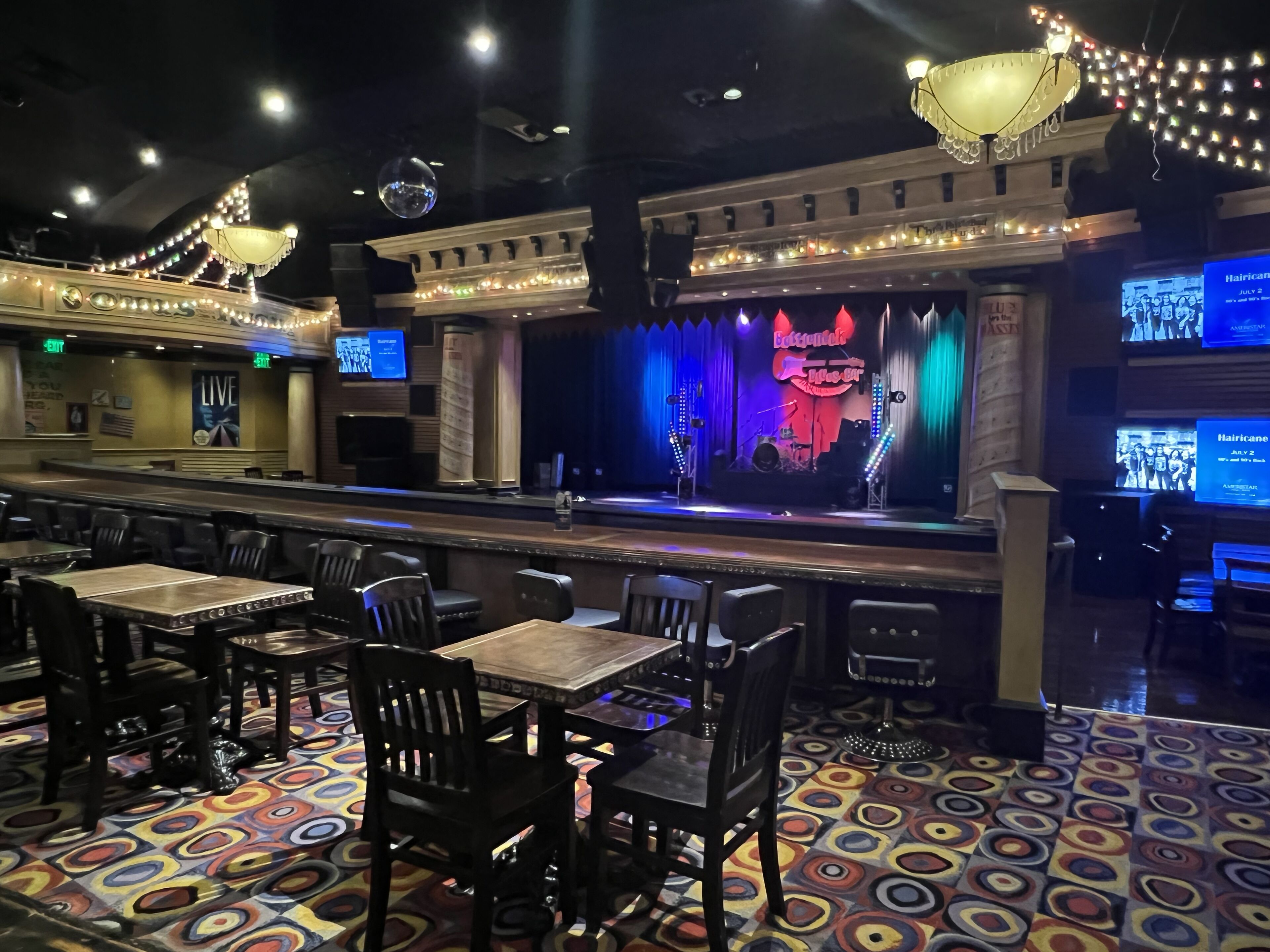 A bar area with tables and chairs, a stage with a band, and a colorful patterned floor.