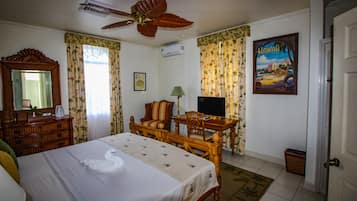 Een hotelkamer met een bed, een houten bureau, een televisie, een plafondventilator en een schilderij van Hawaii.