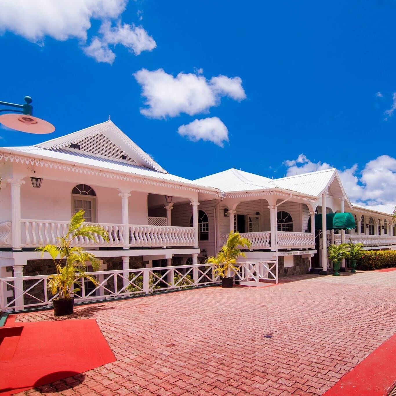Um edifício de estilo colonial branco, com pátio de tijolos vermelhos e grades brancas.