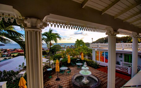 A covered outdoor patio with a fountain, palm trees, and a view of the sea.