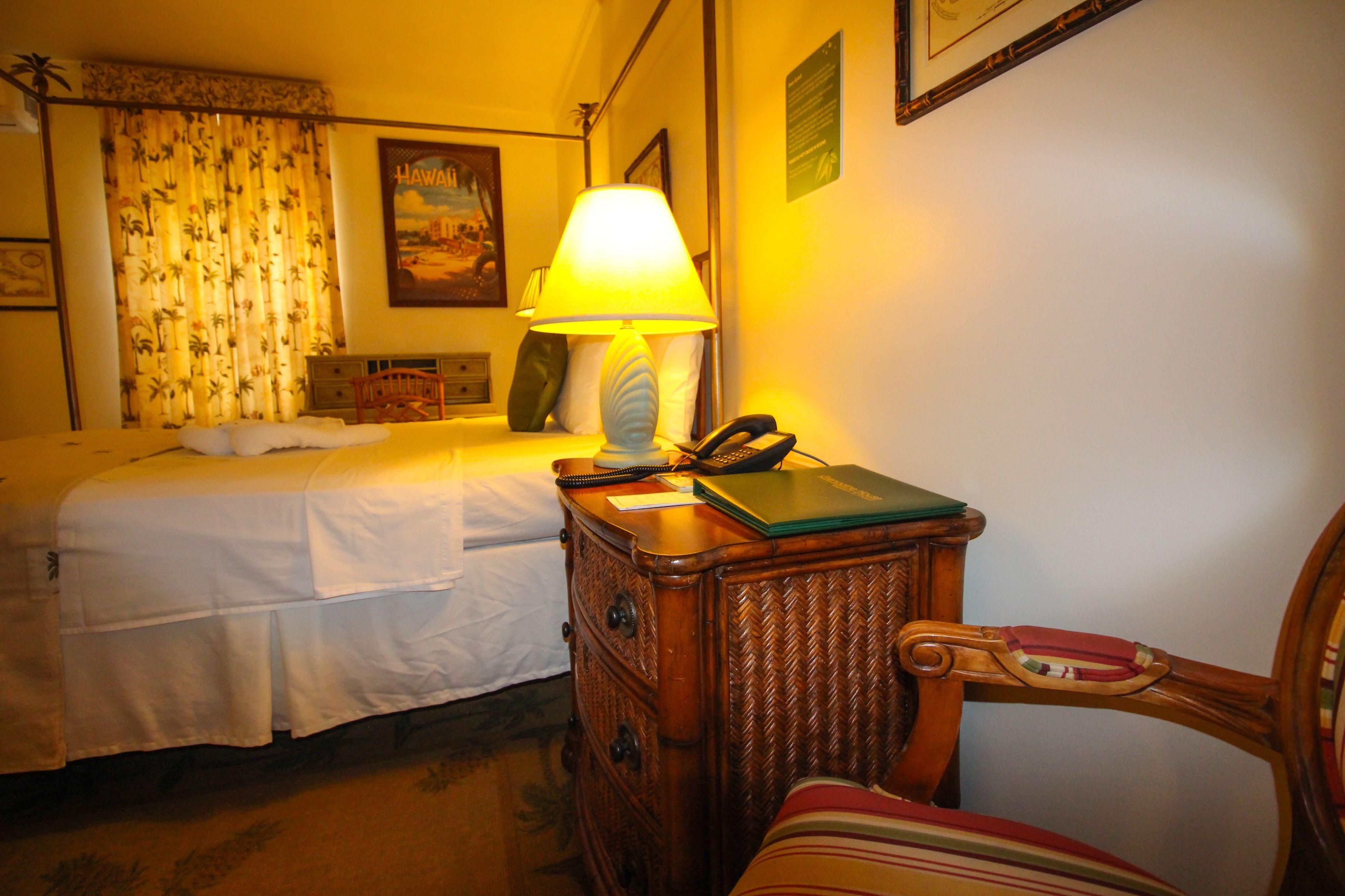 Une chambre d’hôtel avec un lit, une table de chevet avec une lampe, une chaise et une petite table sur laquelle se trouvent un téléphone et un livre.