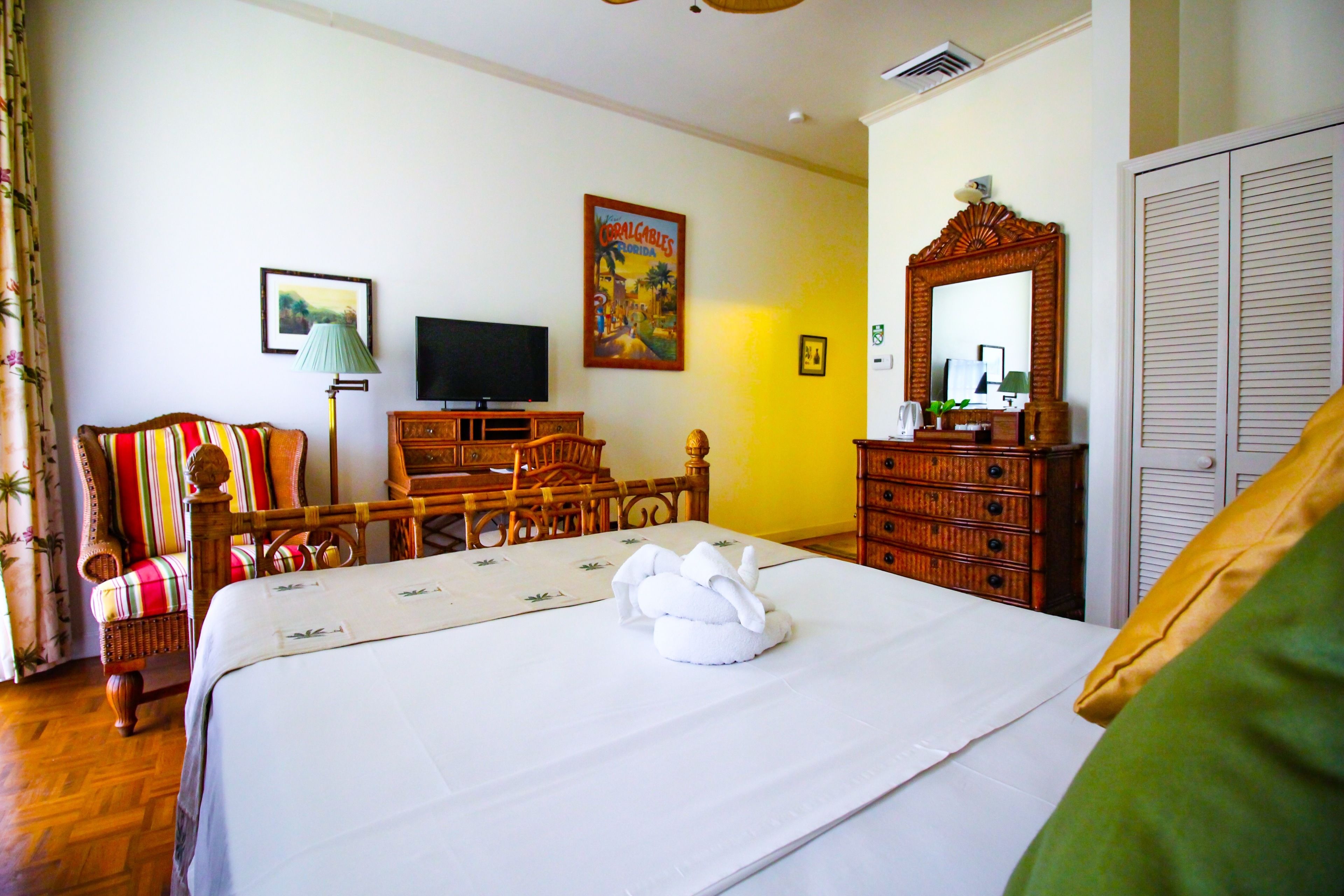 A hotel room with a bed, a television, a wooden dresser, a chair, and a painting on the wall.