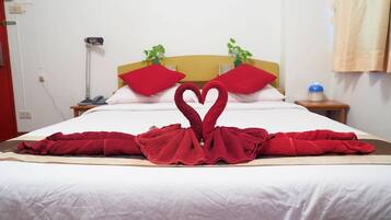 Una cama bien hecha con una disposición de toallas en forma de corazón, un cabecero de madera y una planta en la mesita de noche.