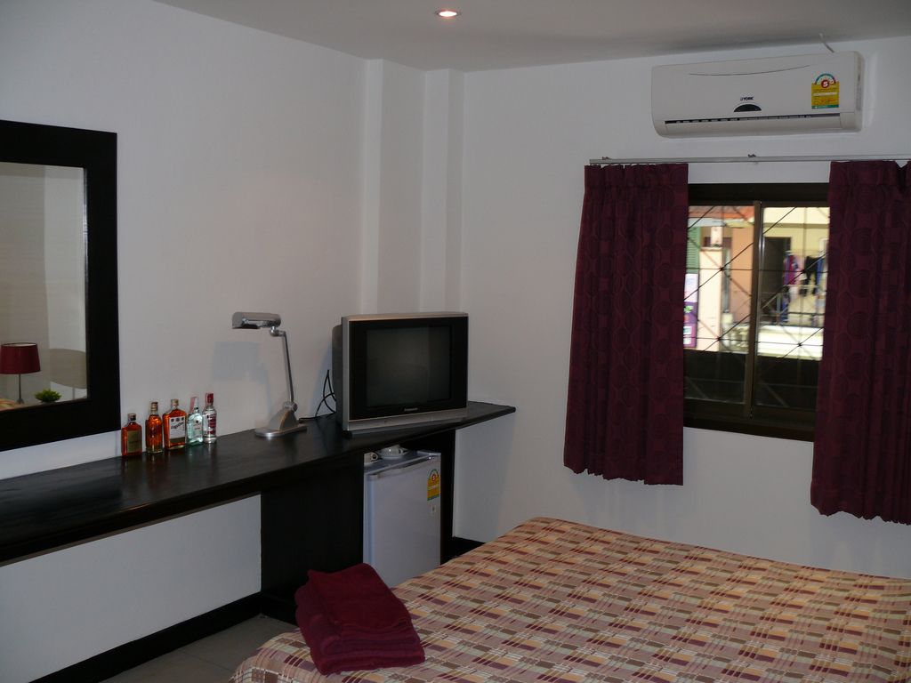 A small room with a bed, a desk with a television, a mirror, and a window with curtains.