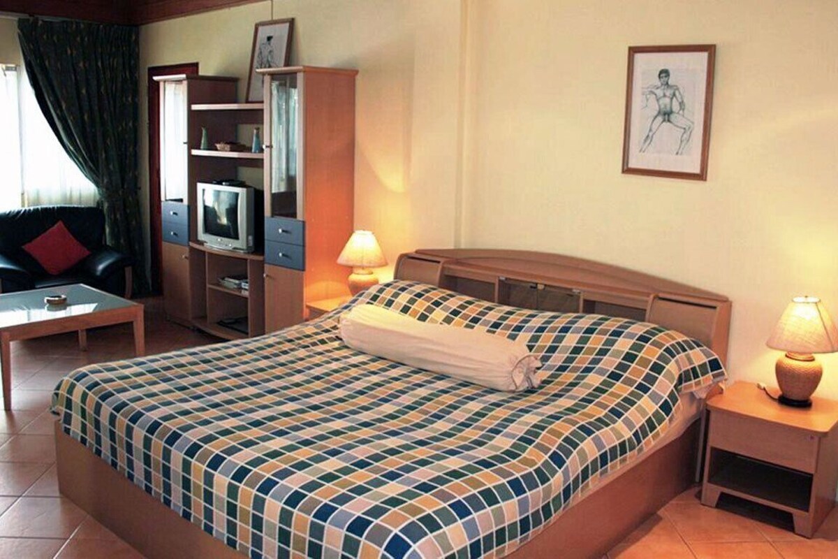Quarto de hotel com cama, televisão, escrivaninha e cadeira.
