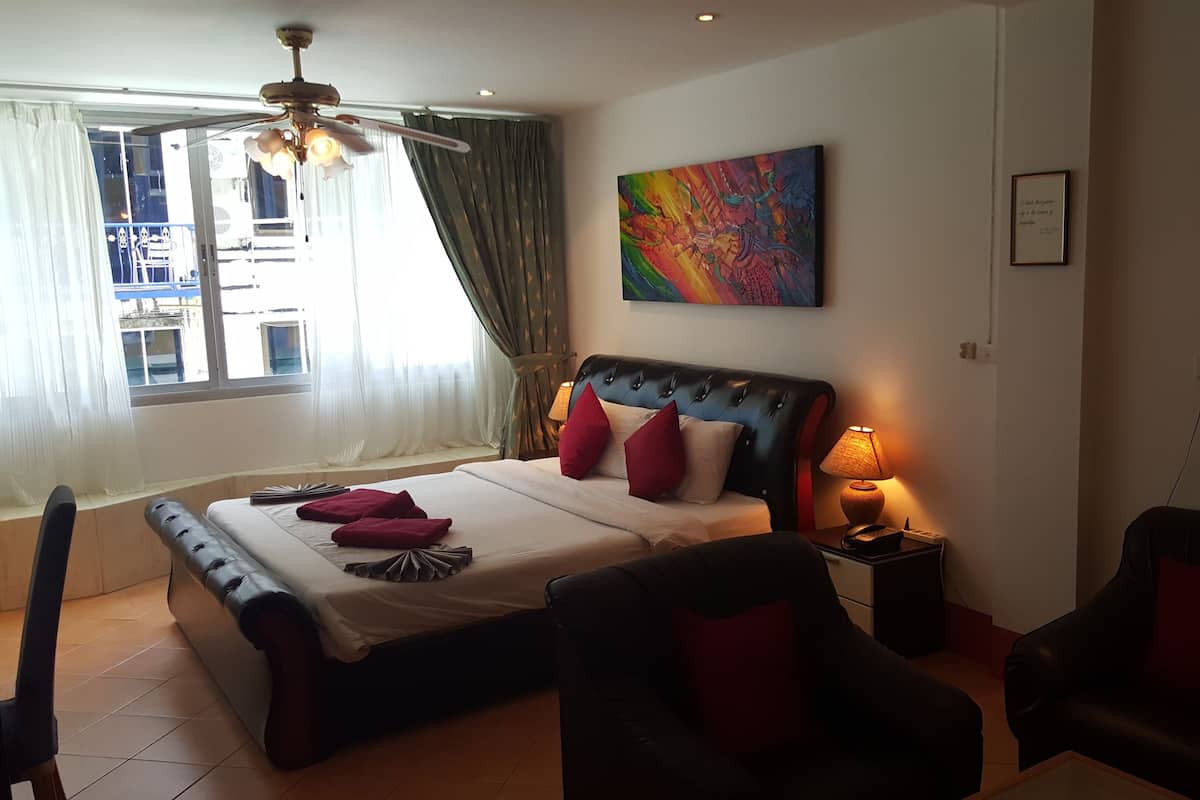 Hotellihuone, jossa on suuri sänky, kattotuuletin, taulu, yöpöytälamppu ja ikkunasta avautuva näkymä ulos.