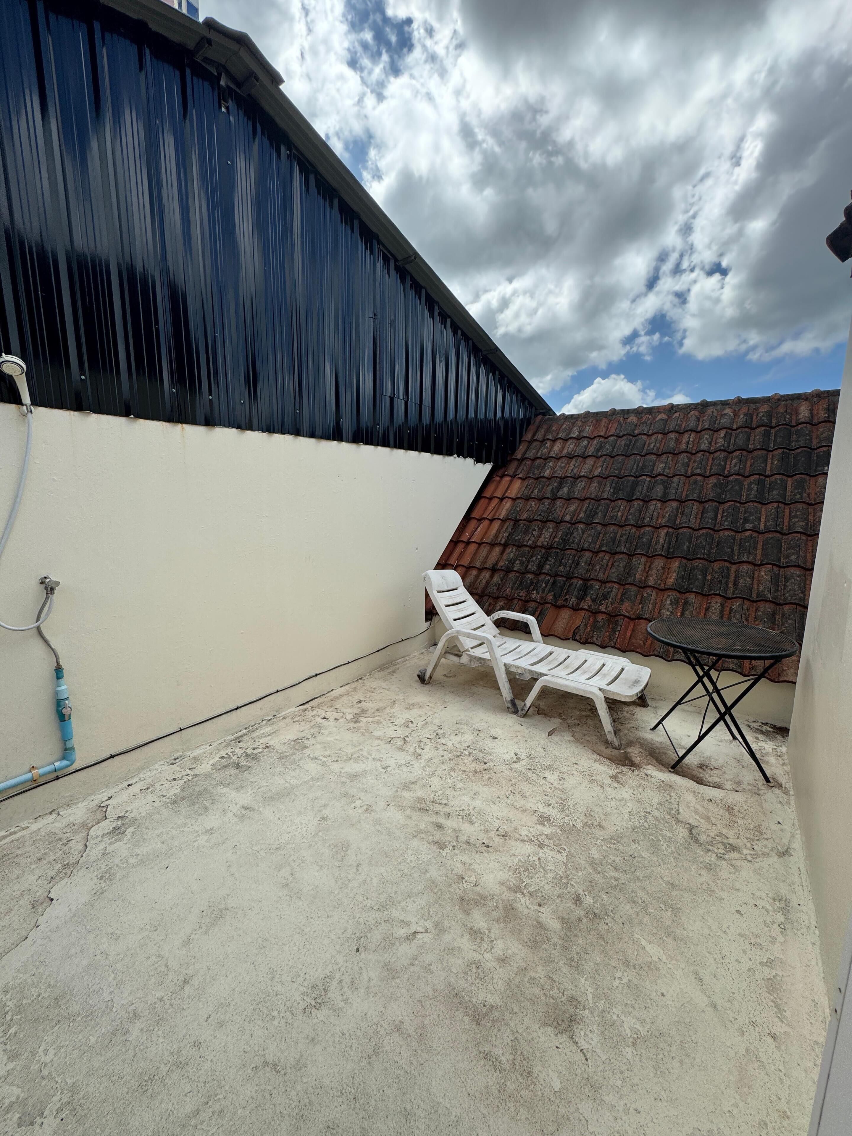 A covered outdoor area with a concrete floor, a white plastic chair, a small round table, and a corrugated metal roof.