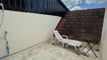 A covered outdoor area with a concrete floor, a white plastic chair, a small round table, and a corrugated metal roof.