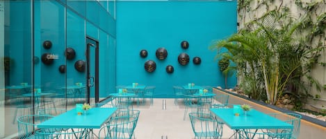 Un comedor moderno con mesas y sillas color turquesa, una pared azul de acento y una maceta con plantas.