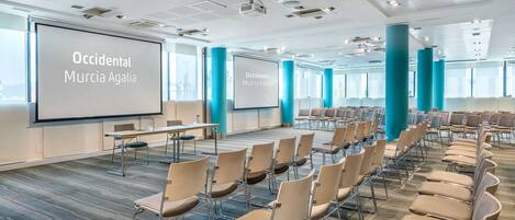 A conference room with rows of chairs, a large screen, and a modern ceiling design.