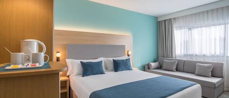 Habitación de hotel con cama, sofá, escritorio con cafetera y mesita de noche.