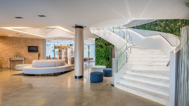 A modern lobby with a curved staircase, a seating area, and a brick wall with a sign.