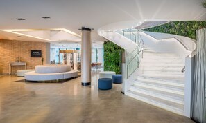 A modern lobby with a curved staircase, a seating area, and a brick wall with a sign.