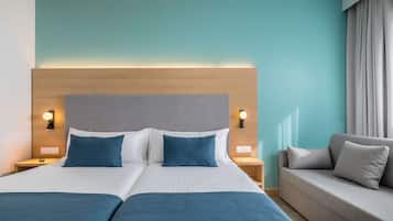 A hotel room with a large bed, two bedside tables, a sofa, and a headboard with integrated lighting.