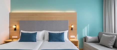 A hotel room with a large bed, two bedside tables, a sofa, and a headboard with integrated lighting.