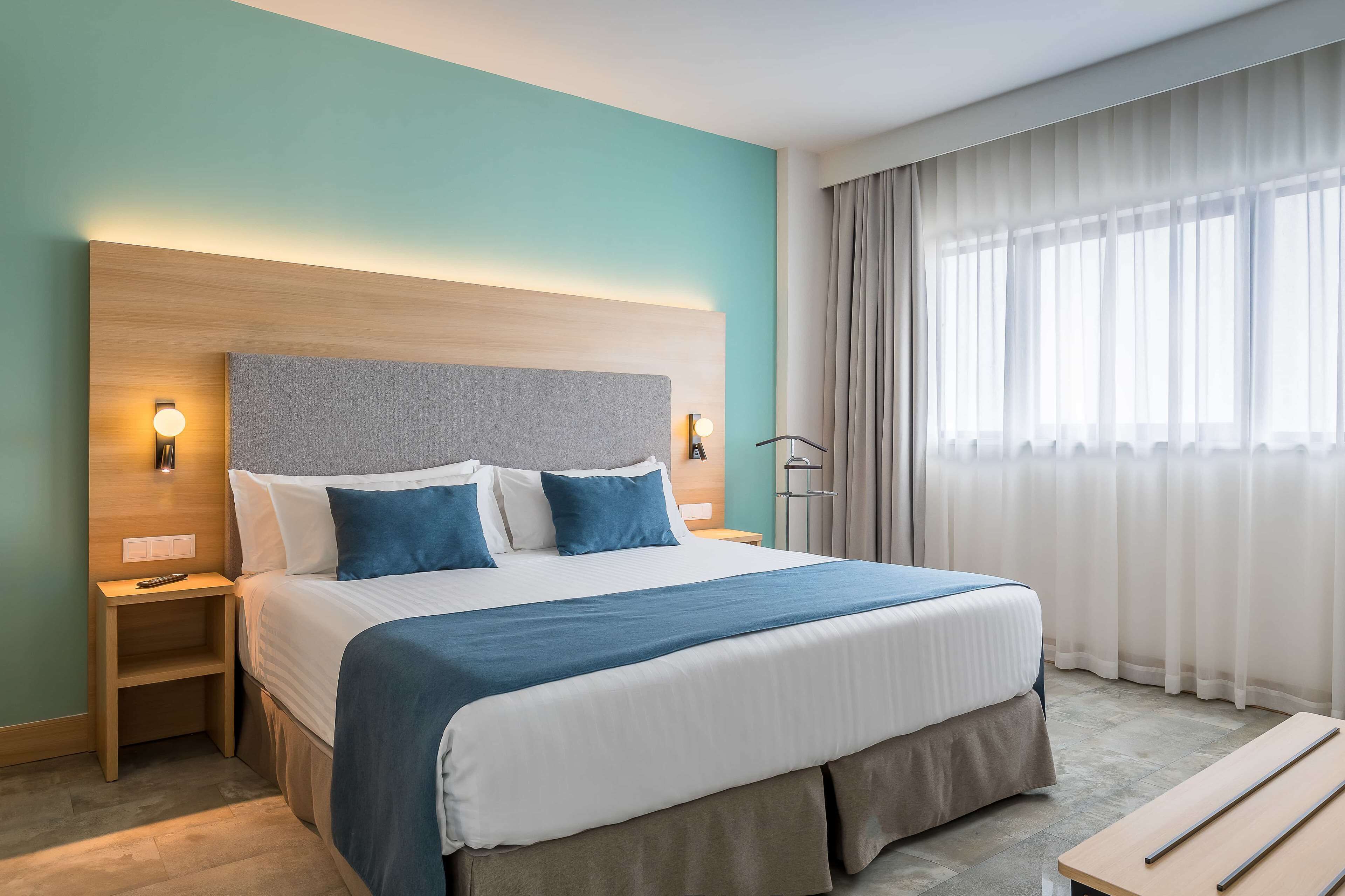 Une chambre d’hôtel avec un grand lit, une table de chevet, un bureau et une fenêtre avec des rideaux.