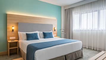 Une chambre d’hôtel avec un grand lit, une table de chevet, un bureau et une fenêtre avec des rideaux.