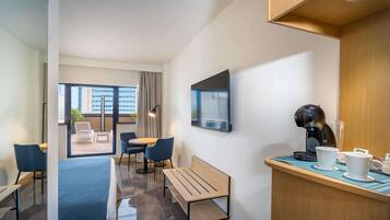 Una habitación de hotel moderna con zona de estar, espacio para café y vistas a la ciudad a través de amplias ventanas.