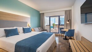 A modern hotel room with a large bed, a seating area with a table and chairs, and a view of the outside through large windows.