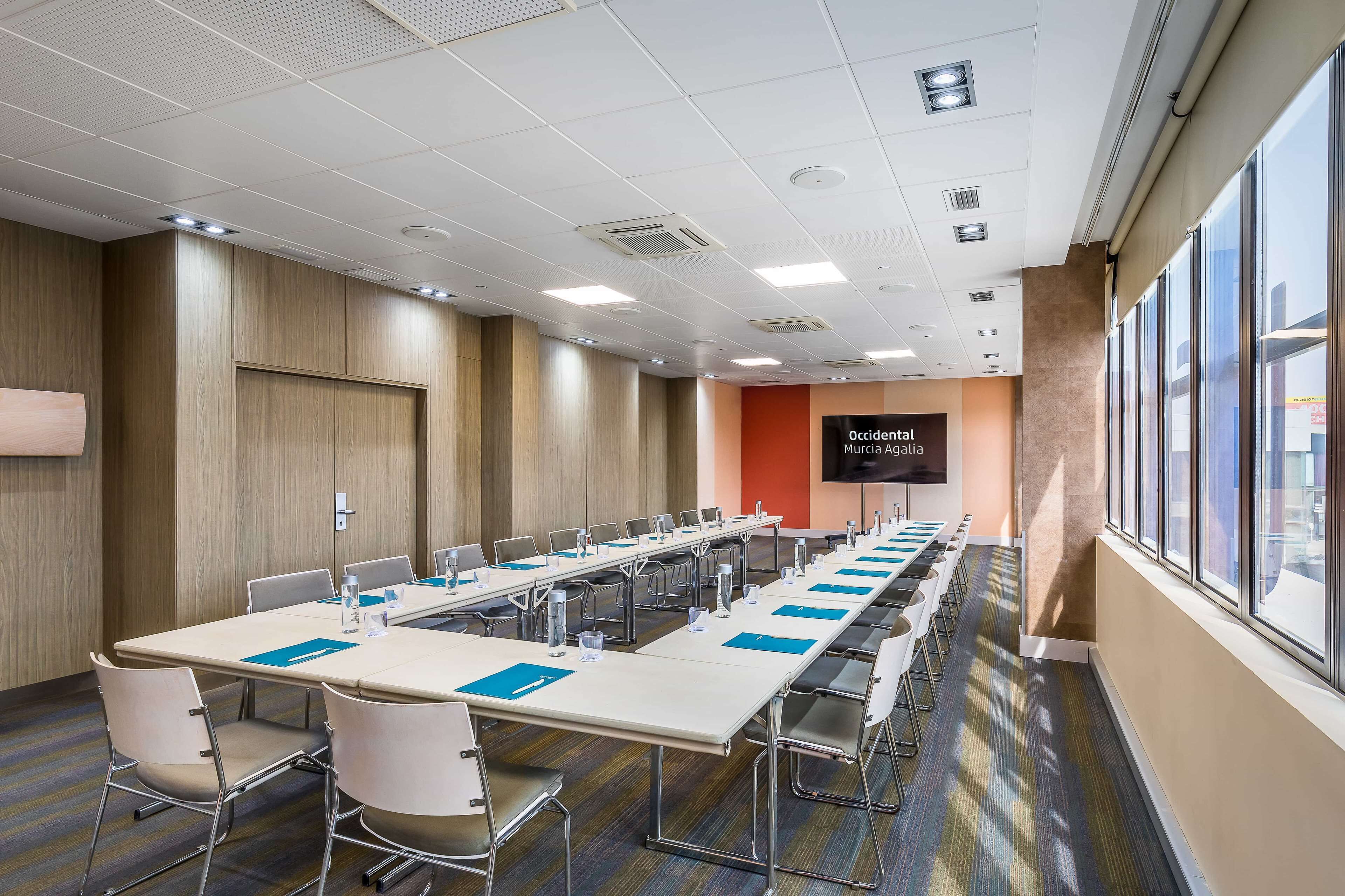 Une salle de conférence avec une longue table, des chaises et un écran affichant le texte « Agence de marketing par hasard ».