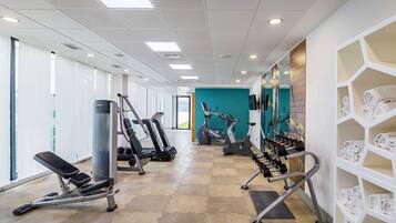 Un gimnasio con equipo de ejercicio, una banca y una pared con toallas.