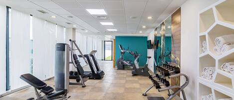 A gym with exercise equipment, a bench, and a wall with towels.