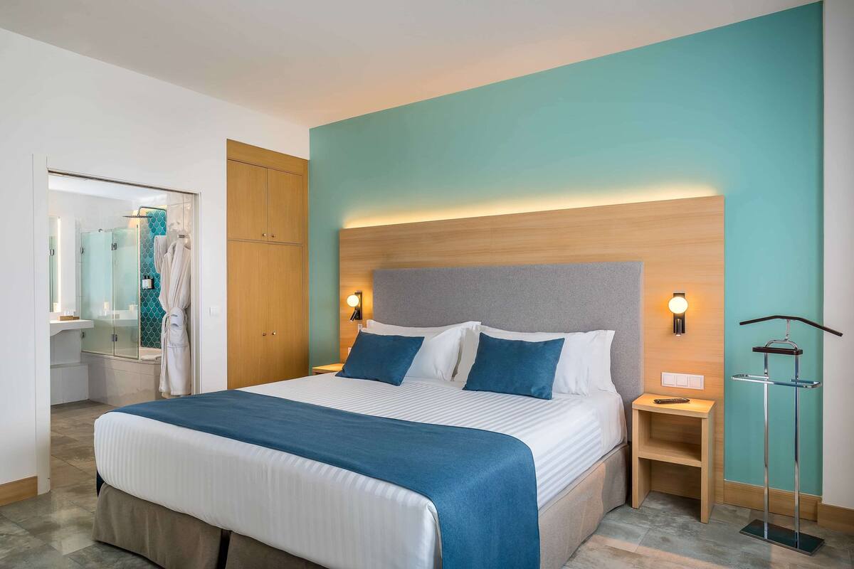 A hotel room with a bed, bedside tables, a wardrobe, and a bathroom visible through an open door.