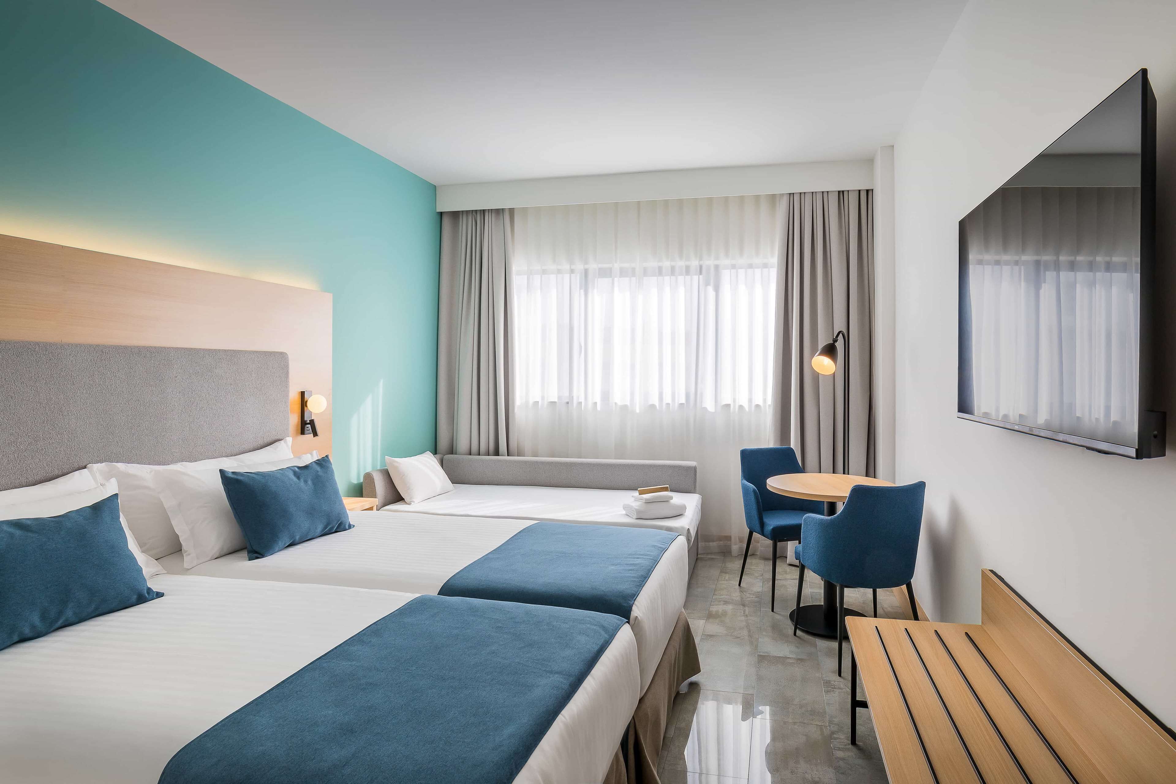 Habitación de hotel con dos camas, un sofá, un escritorio y una televisión.