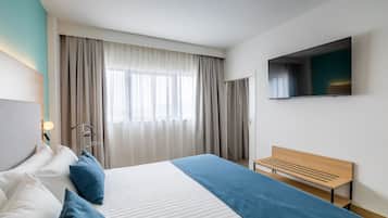 Habitación de hotel moderna con una cama grande, un banco de madera, un televisor de pantalla plana y un ventanal con cortinas.