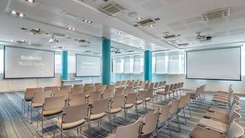 Un salón de conferencias con hileras de sillas, una pantalla grande y un proyector.