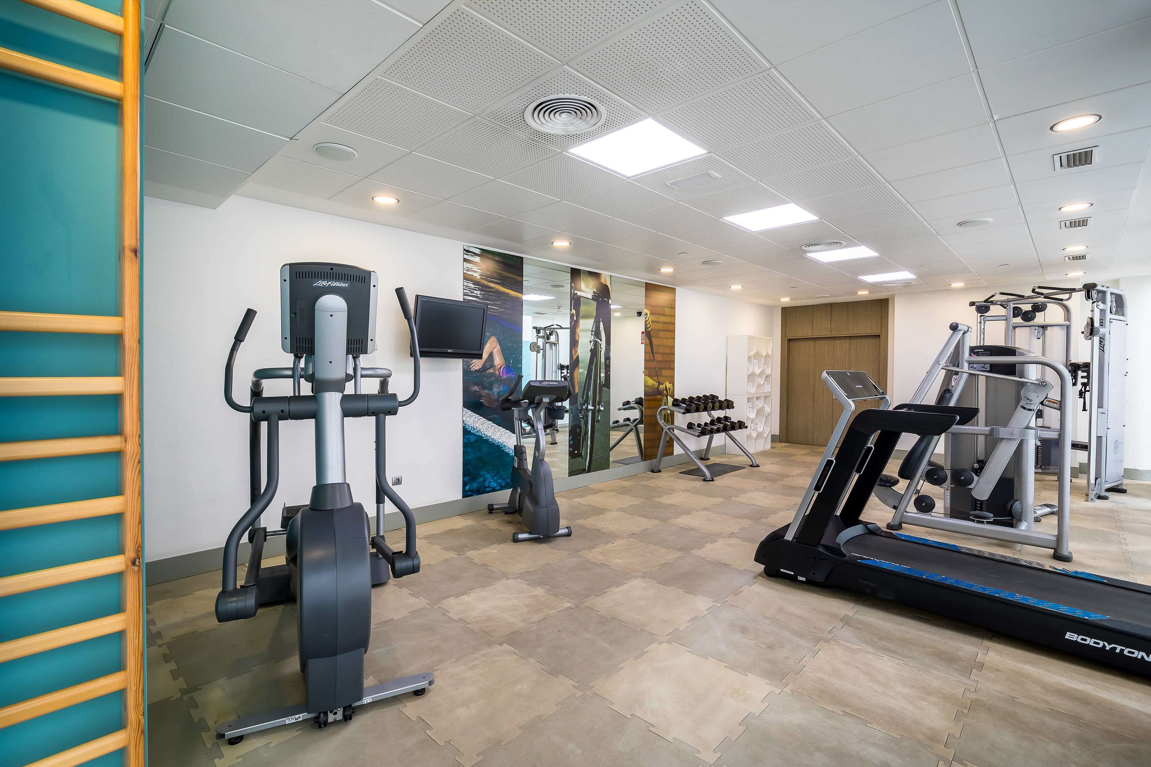 Une salle de sport équipée de machines de cardio, de postes d’entraînement avec poids et d’un tapis de course.