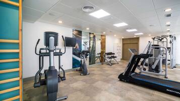 Une salle de sport équipée de machines de cardio, de postes d’entraînement avec poids et d’un tapis de course.