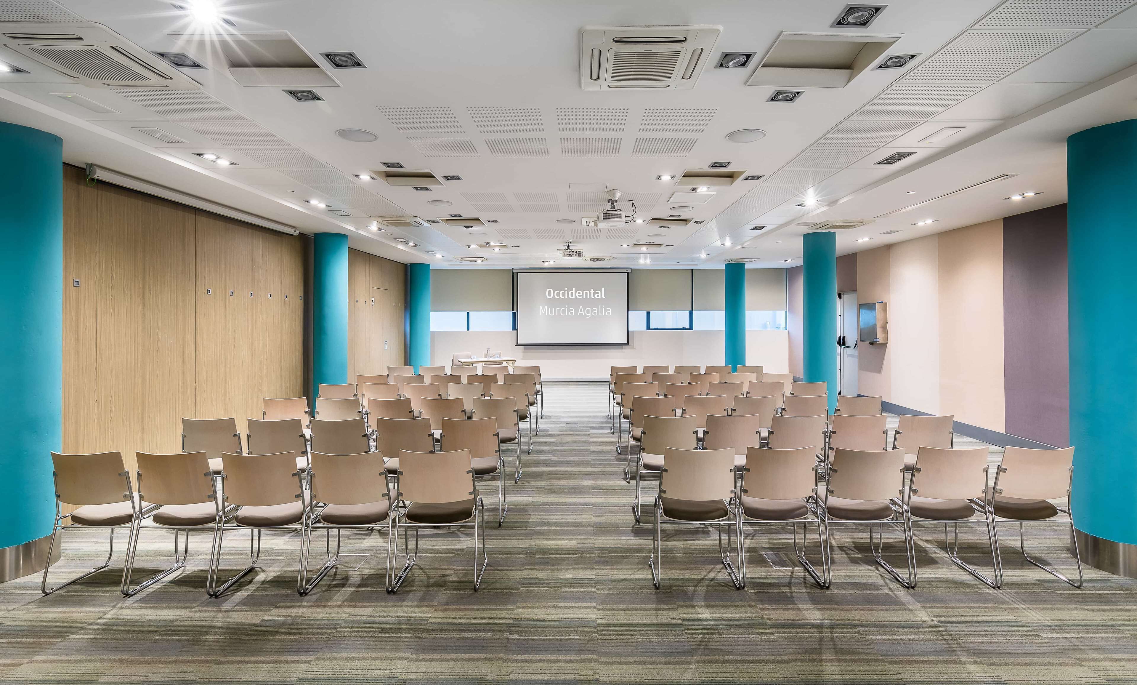 A conference room with rows of chairs, a large screen, and a projector.