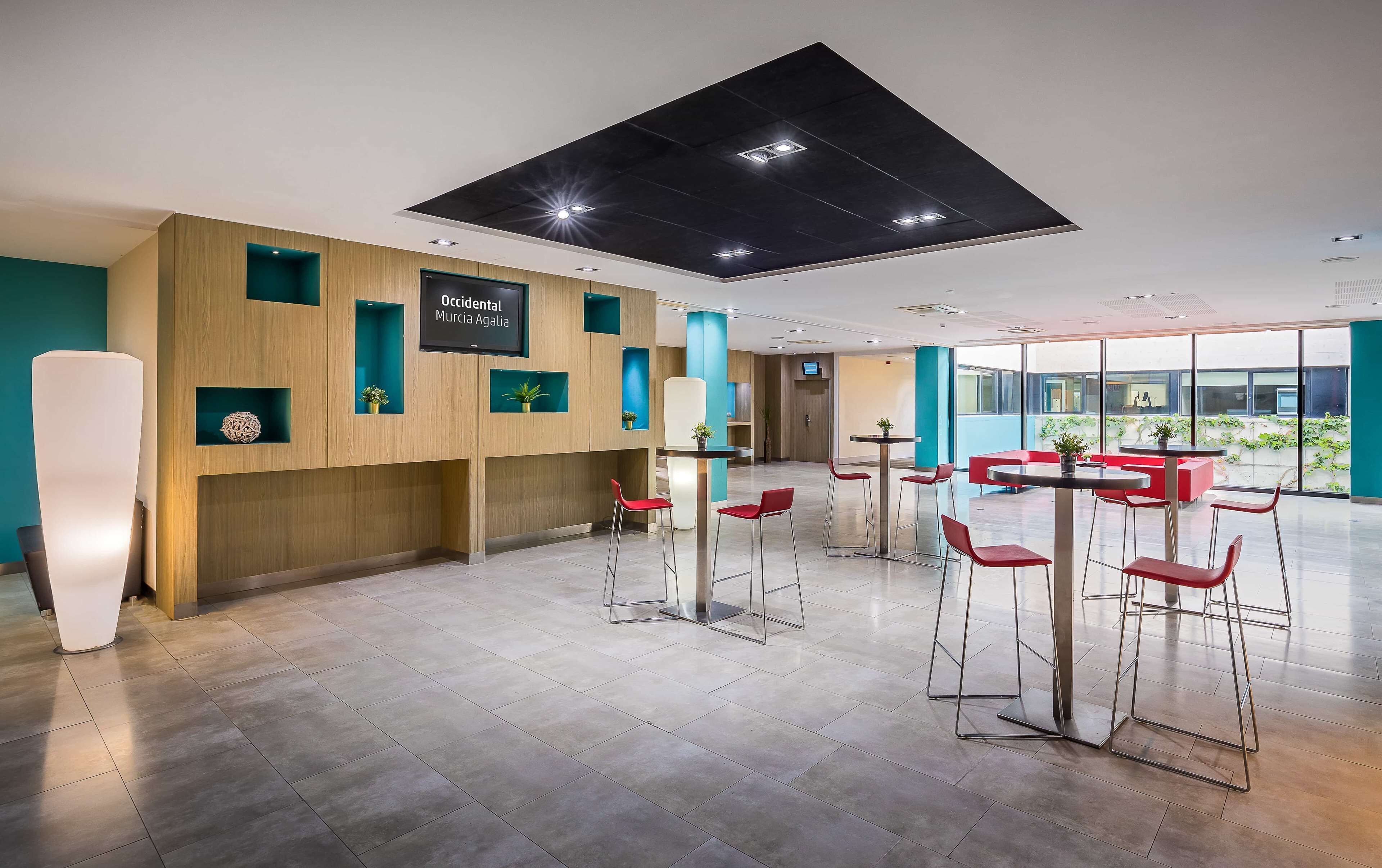 A modern interior with a reception desk, red bar stools, and a large window offering a view of the outdoors.