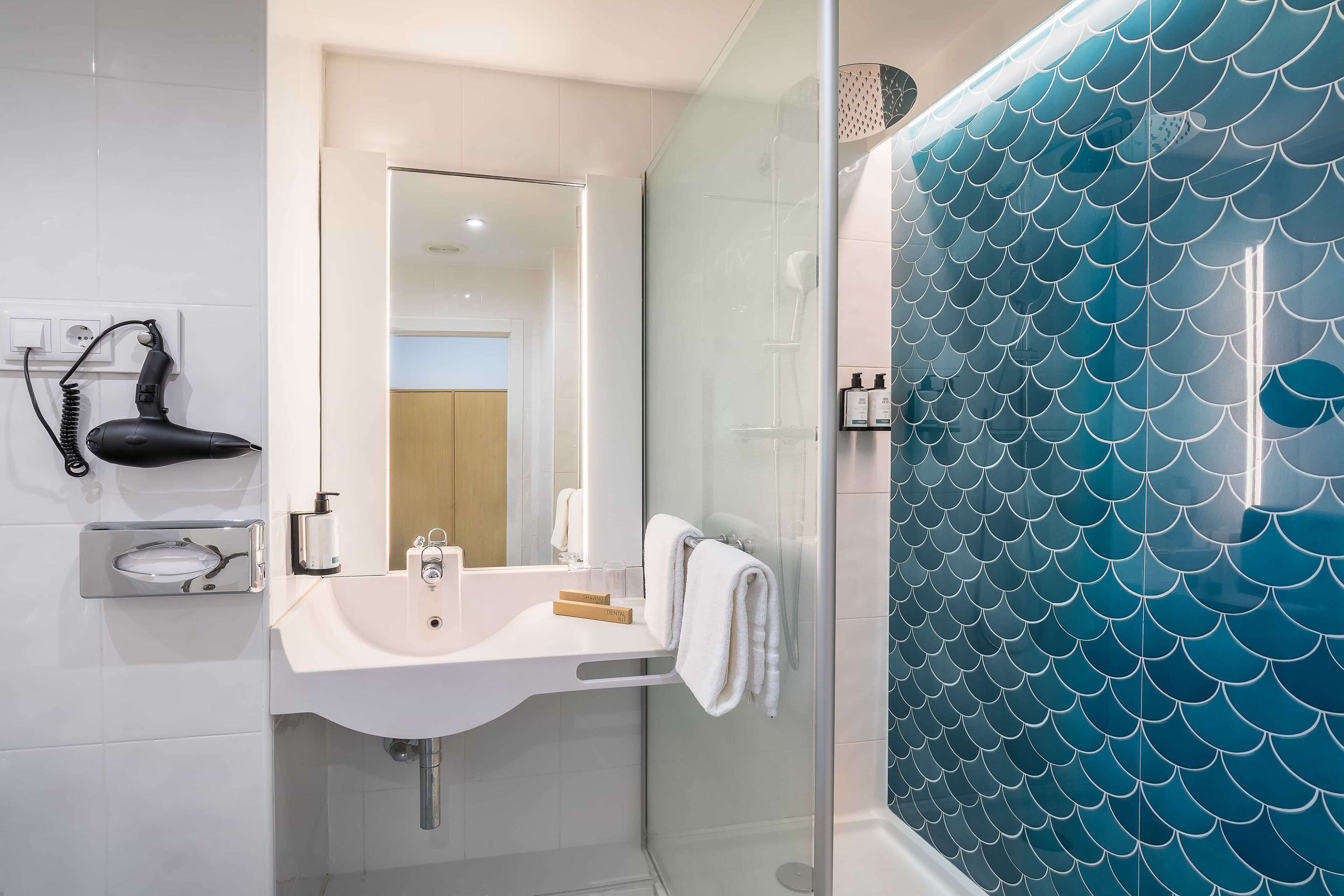 A modern bathroom with a white sink, mirror, and glass-enclosed shower with blue tiles.