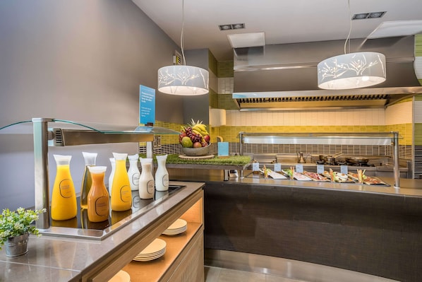 A buffet area with a variety of food and drink options, including juices, fruits, and a selection of dishes.