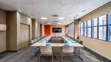 A conference room with a long table, chairs, a screen, and large windows.