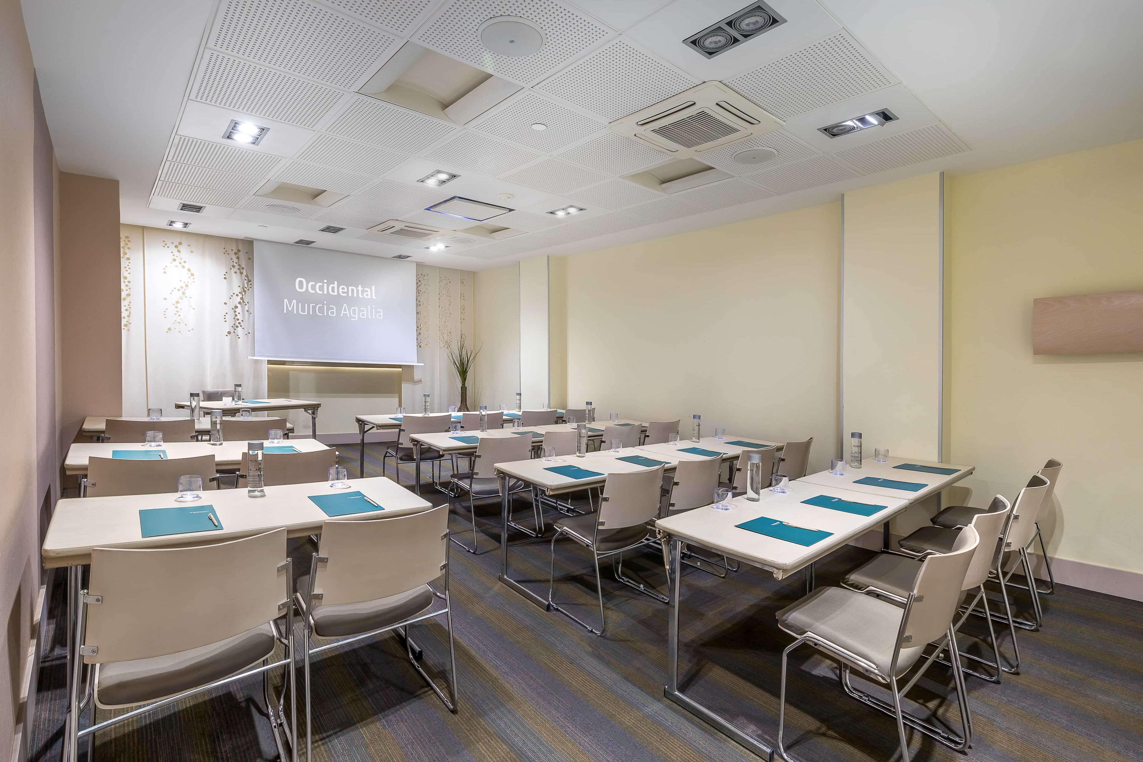 A conference room with multiple tables and chairs, equipped with water bottles and notepads.