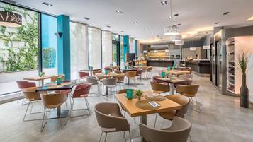 A modern restaurant with multiple tables and chairs, large windows, and a visible kitchen area.
