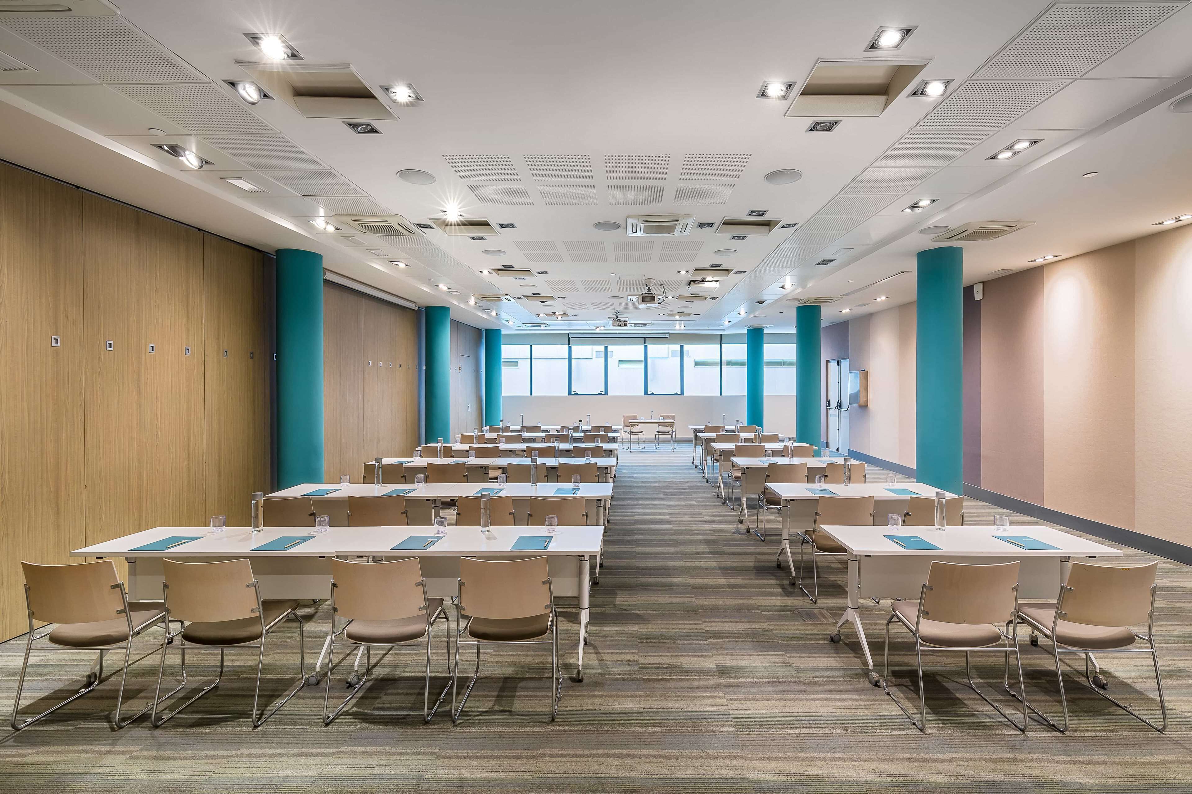 A conference room with rows of tables and chairs, large windows, and a modern ceiling design.
