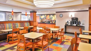 A restaurant with booths and tables, a colorful carpet, and a counter with a clock and coffee machines. - Fairfield Inn & Suites by Marriott Asheboro (Asheboro)