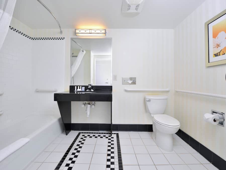 Ein modernes Badezimmer mit einem schwarz-weißen Schachbrettfußboden, einer weißen Toilette, einem schwarzen Waschbecken und einem Duschbereich.