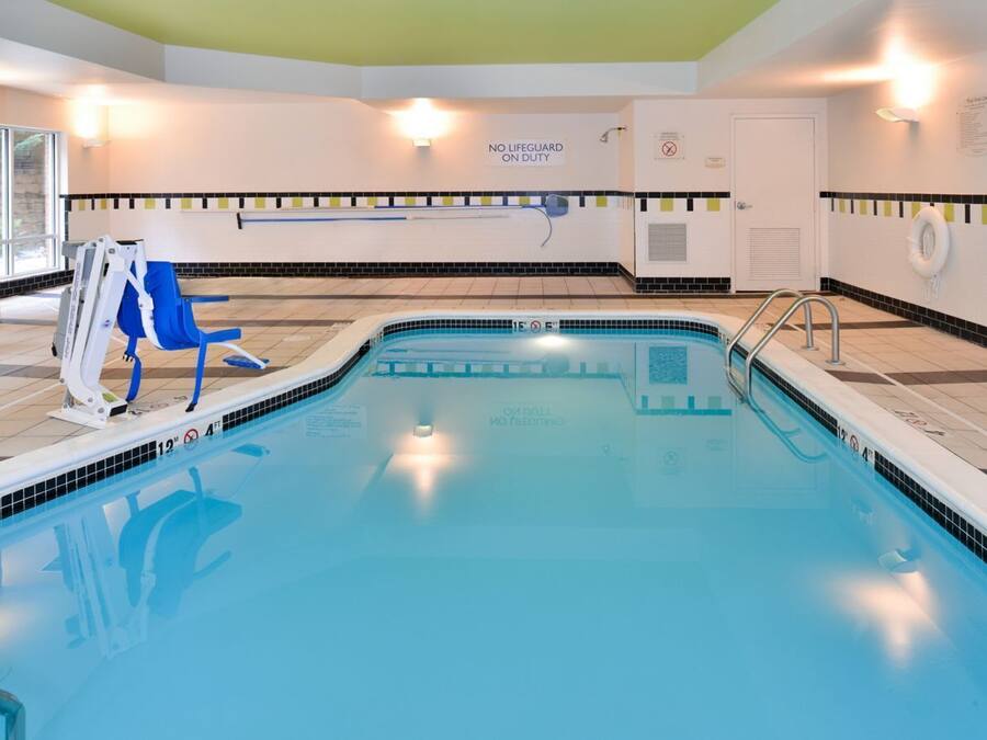 An indoor swimming pool with a lifeguard chair, a pool ladder, and safety signs.