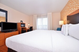 Habitación de hotel con una cama grande, televisión, escritorio con silla, microondas y ventana con cortinas.