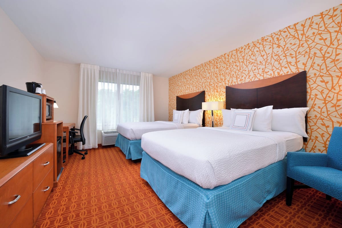 A hotel room with two beds, a desk with a chair, a television, and a patterned wall.