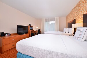 A hotel room with a bed, a desk with a television, and a window with curtains.