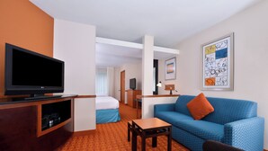 A hotel room with a TV, a blue sofa, a small table, a bed, and a desk with a lamp. - Fairfield Inn & Suites by Marriott Asheboro (Asheboro)