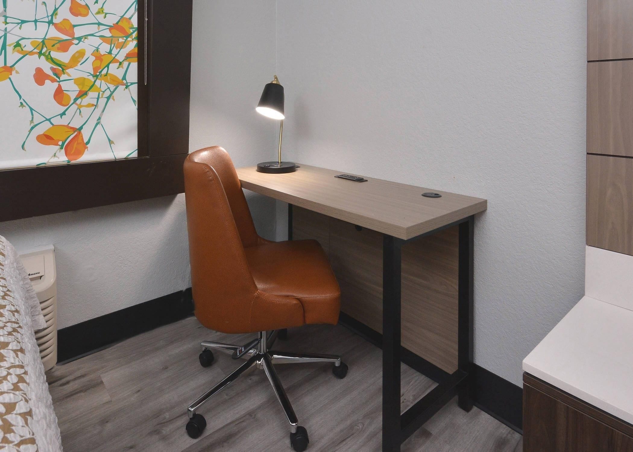 Et lille, moderne værelse med et træskrivebord, en læderstol og en skrivebordslampe.