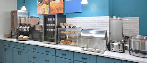 A breakfast bar with a coffee machine, waffle maker, and toaster. There are also cabinets and a yellow chair.